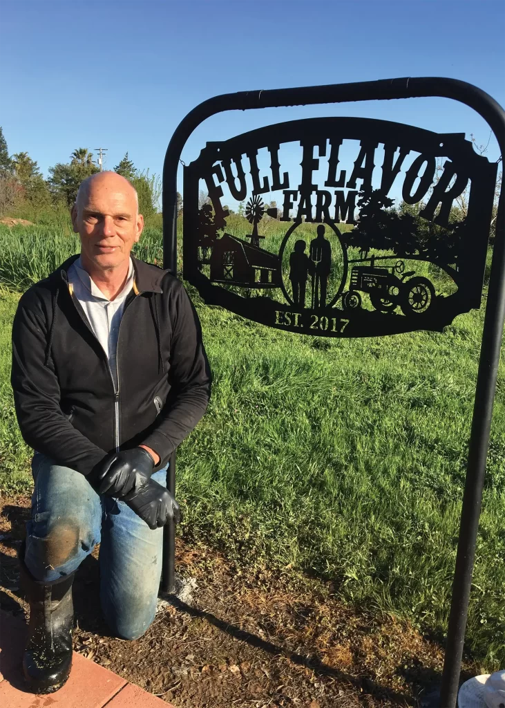 A farmer posing for a photo in front of the Full Flavor Farm sign.