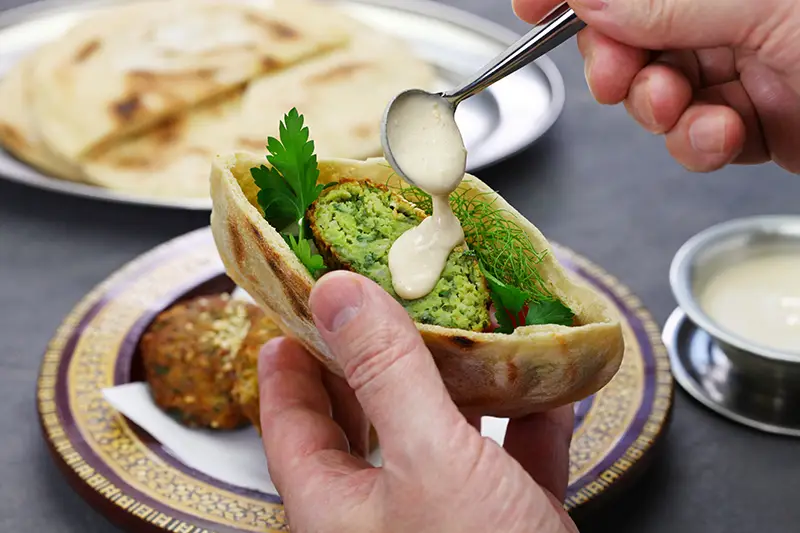 A person drizzling sauce on a pita stuffed with falafel.