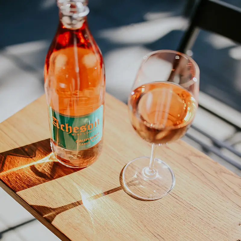Acheton wine bottle on table with a glass of wine